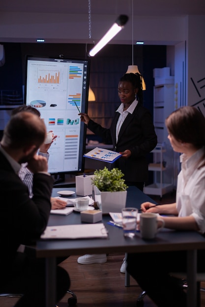 Foto mulher de negócios com pele escura explicando gráficos financeiros usando o monitor de apresentação