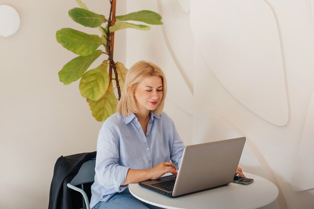 Mulher de negócios com uma camisa azul, trabalhando em um notebook em um café em uma mesa branca