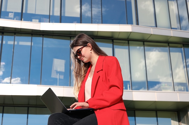 Mulher de negócios com uma jaqueta trabalhando com um laptop no contexto de um prédio de escritórios