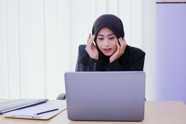 Mulher de negócios confusa usando um laptop enquanto se senta à mesa no escritório