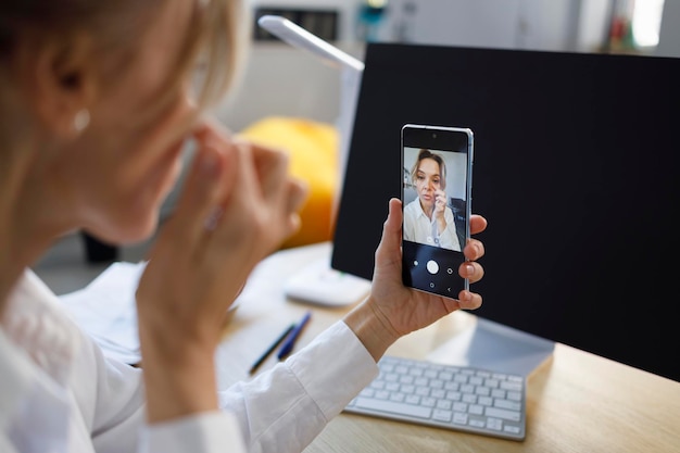 Foto mulher de negócios corrigindo maquiagem olhando para a câmera do smartphone