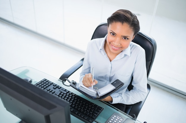 Mulher de negócios de cabelo escura nova feliz que toma notas em sua programação