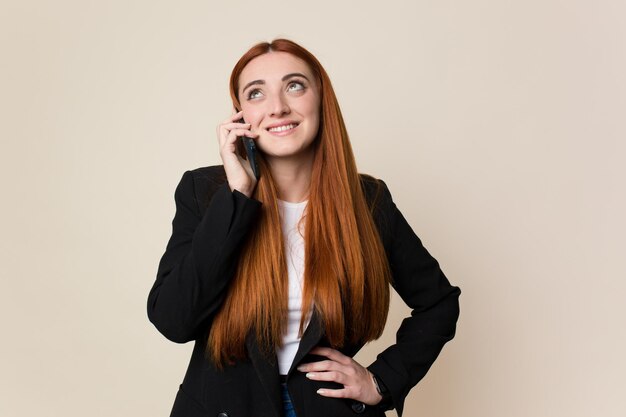 Mulher de negócios de cabelo vermelho jovem usando seu telefone celular isolado