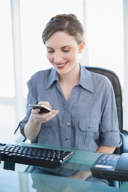 Mulher de negócios de conteúdo usando seu smartphone sentado em sua mesa