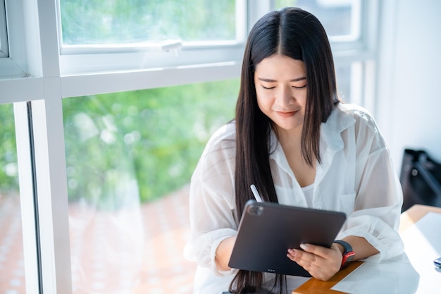 Mulher de negócios de freelancers asiáticos usando smartwatch falando usando casual trabalhando com tablet para navegar na internet conversando e blogando e smartphonenotebook no café