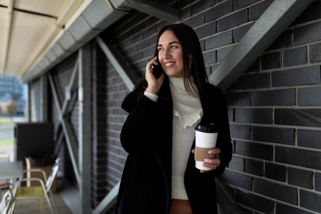 Mulher de negócios de meia-idade falando em um telefone celular com uma xícara de café nas mãos do lado de fora
