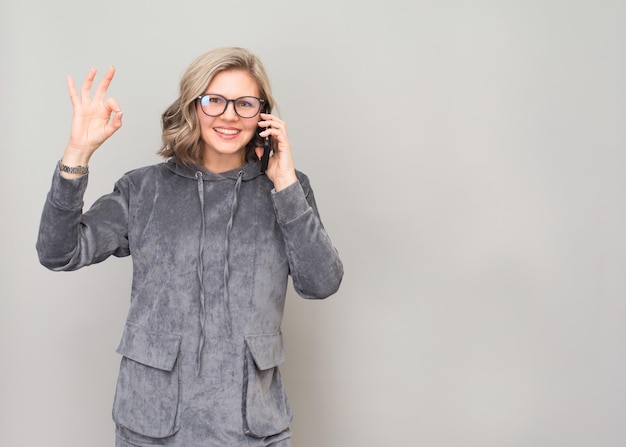 Mulher de negócios de meia idade sorridente em óculos com smartphone mostrando gesto okey