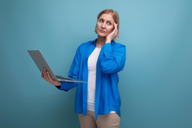 Mulher de negócios de meia idade trabalhando como freelancer com laptop em fundo azul com espaço de cópia