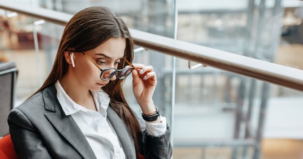 Mulher de negócios de óculos no local de trabalho usa o telefone e se senta à mesa