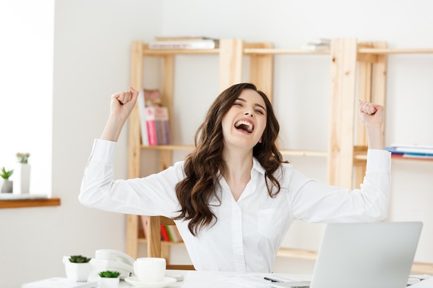 Mulher de negócios de sucesso com os braços erguidos, sentada em um escritório moderno