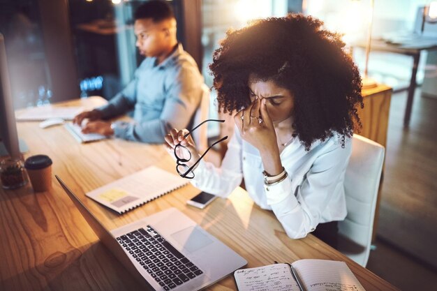 Mulher de negócios e dor de cabeça de tensão ocular na mesa com estresse excesso de trabalho e prazo de trabalho à noite funcionários profissionais e fadiga no escritório de coworking com esgotamento internet glitch e dor