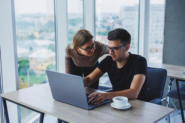 Mulher de negócios e empresário estão procurando algo no laptop O conceito de cooperação empresarial e trabalho em equipe Jovens millennials sorridentes à mesa no escritório Pessoas modernas de sucesso