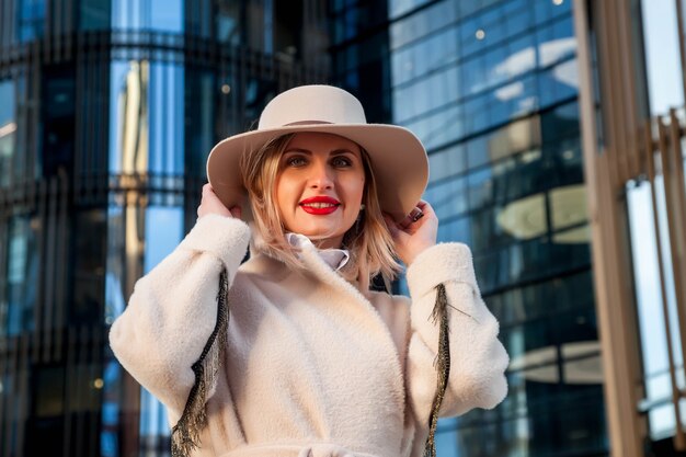 Mulher de negócios elegante ao ar livre contra o centro de negócios. Mulher de jaleco branco e chapéu no distrito financeiro