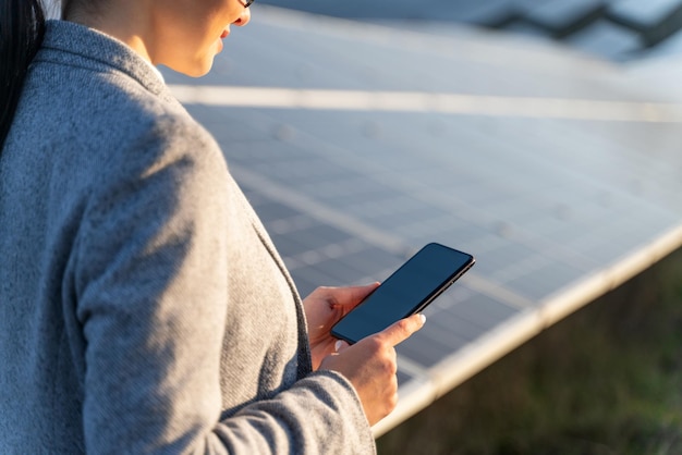 Mulher de negócios elegante com roupa formal com smartphone em frente às baterias de energia ao ar livre