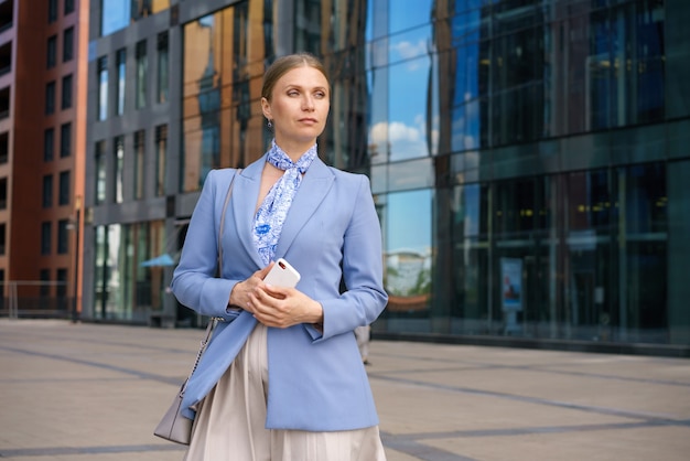 Mulher de negócios elegante com uma jaqueta azul e um telefone na mão fica no centro de negócios