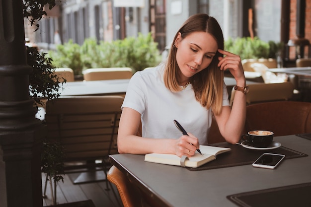 Mulher de negócios elegante em um café de rua fazendo anotações em um caderno