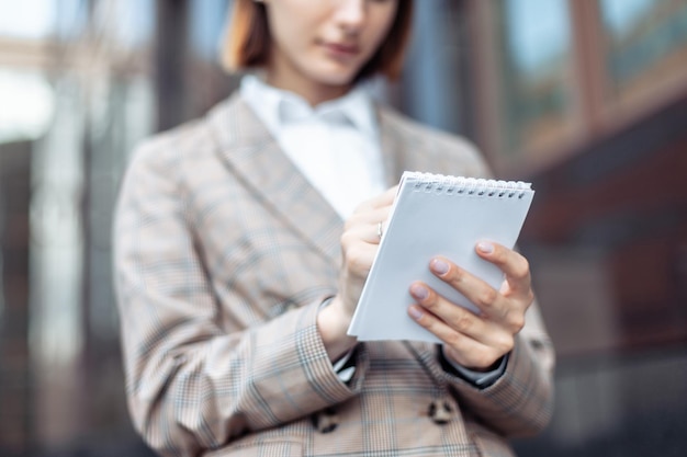 Mulher de negócios elegante jovem anota informações importantes em um notebook no contexto de um edifício comercial