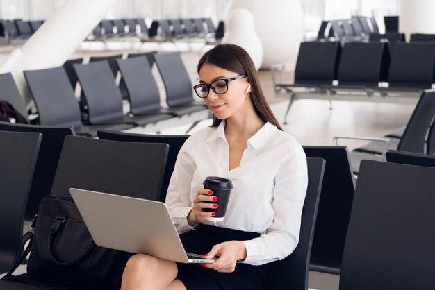 Foto mulher de negócios elegante jovem no terminal do aeroporto internacional, trabalhando em seu laptop enquanto aguarda o voo