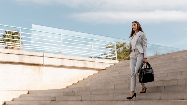 Foto mulher de negócios elegante na escada ao ar livre com bolsa e espaço de cópia