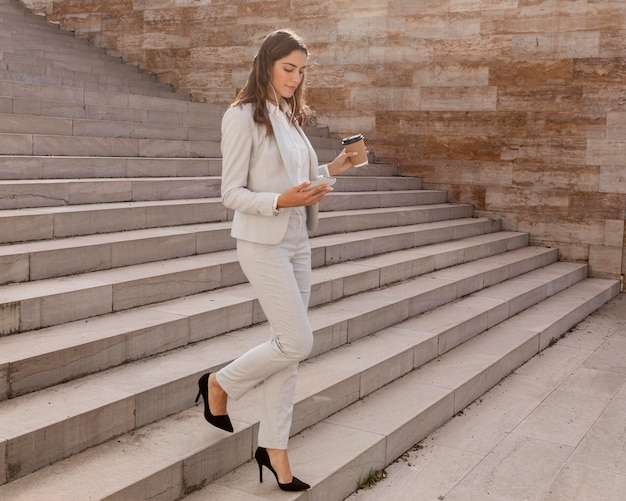 Foto mulher de negócios elegante na escada ao ar livre com smartphone e café