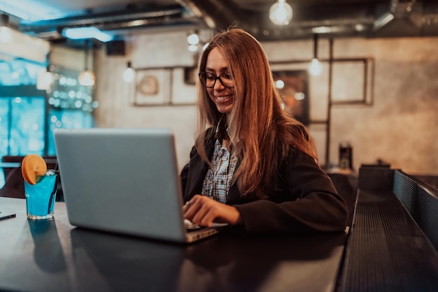 Mulher de negócios em copos sentado em um café moderno e trabalhando em seu laptop enquanto bebe um coquetel Foco seletivo