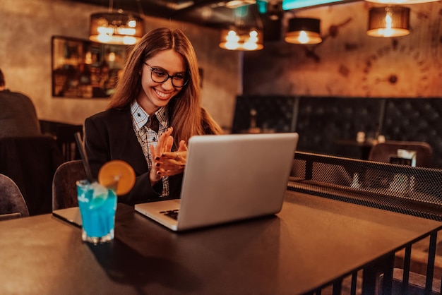 Mulher de negócios em copos sentado em um café moderno e trabalhando em seu laptop enquanto bebe um coquetel Foco seletivo