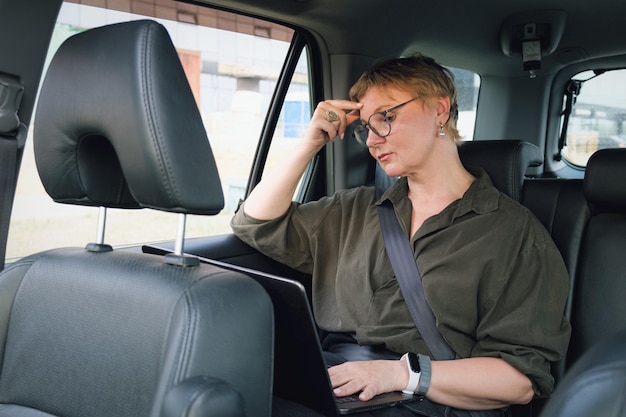 Mulher de negócios em óculos está falando ao telefone enquanto está sentado no banco de trás de um carro