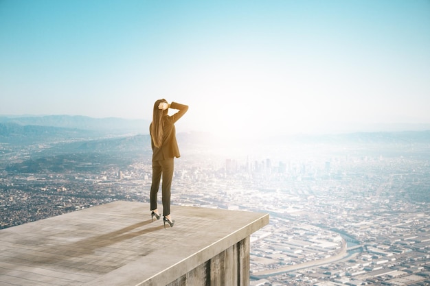 Mulher de negócios em um telhado de concreto abstrato olhando para o horizonte da cidade e a vista do céu com um modelo de lugar de crescimento de sucesso carreira futura e conceito de amanhã