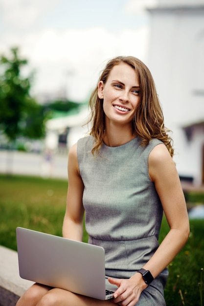 Mulher de negócios em um vestido elegante usando laptop na rua