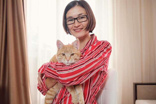 Mulher de negócios em uma camisa vermelha com um gato ruivo em casa