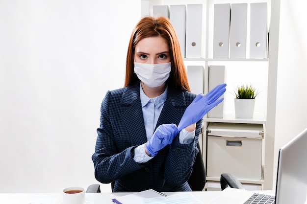 Mulher de negócios em uma máscara no local de trabalho coloca luvas de borracha