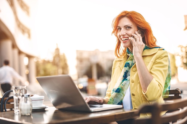 Mulher de negócios está trabalhando no laptop e usando smartphone em uma pausa para o café em um café de rua.