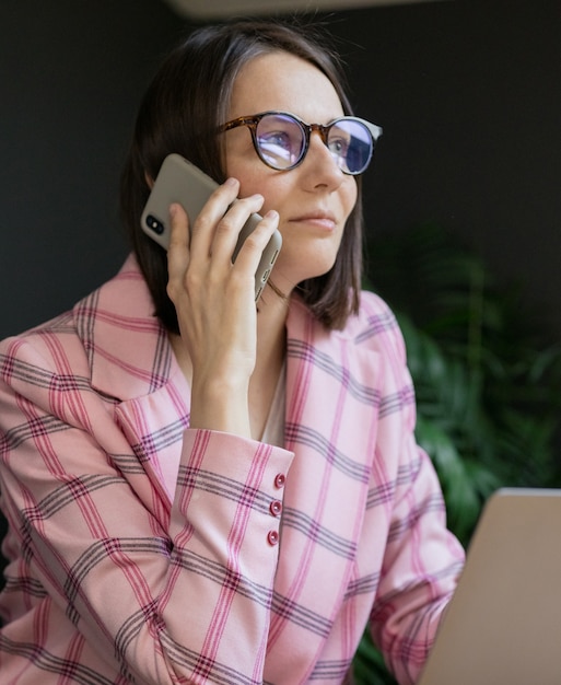 Mulher de negócios europeia confiante com uma jaqueta rosa e um laptop no escritório trabalhando