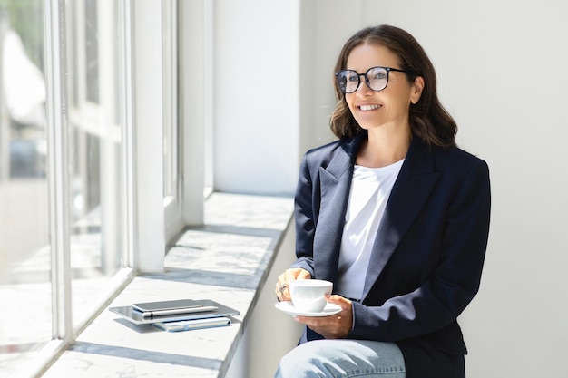 Foto mulher de negócios europeia de meia-idade positiva com telefone bebendo café