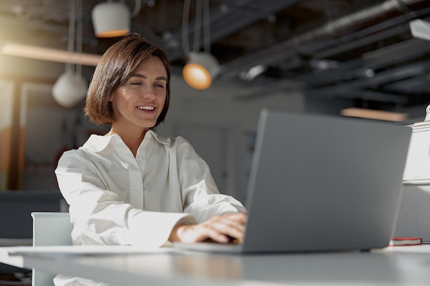 Mulher de negócios europeia sorridente trabalhando em laptop enquanto está sentada em um café aconchegante