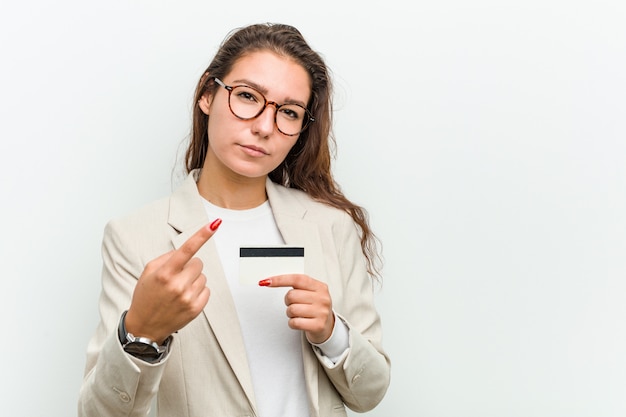 Mulher de negócios europeu jovem segurando um cartão de crédito, apontando com o dedo para você, como se convidando se aproximar.