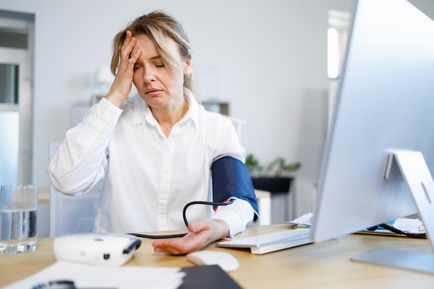 Mulher de negócios exausta medindo sua pressão arterial e pulso no local de trabalho