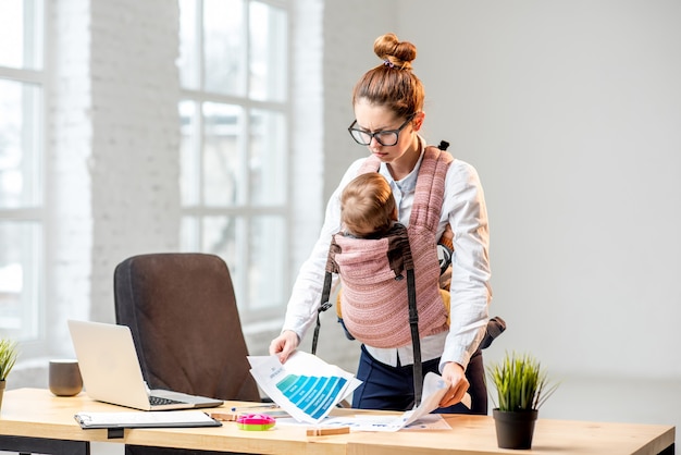 Mulher de negócios exausta trabalhando com documentos em papel com seu filho bebê no escritório