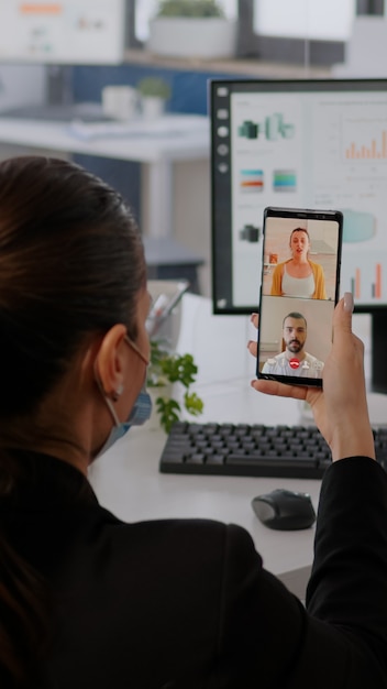 Foto mulher de negócios executiva usando máscara protetora usando telefone para videochamada online