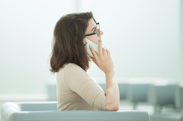 Mulher de negócios falando em um smartphone sentada na sala do escritório