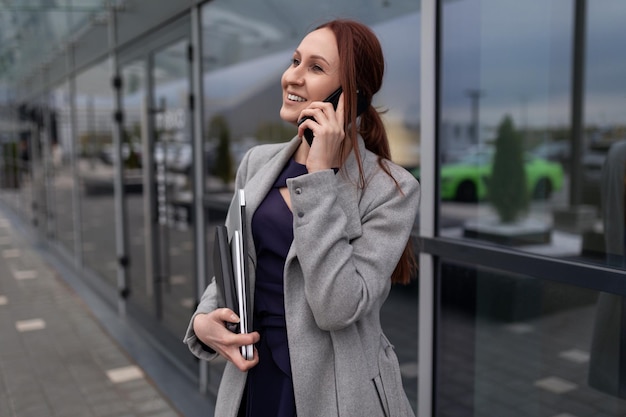 Mulher de negócios falando em um telefone celular com um laptop nas mãos ao lado da entrada do