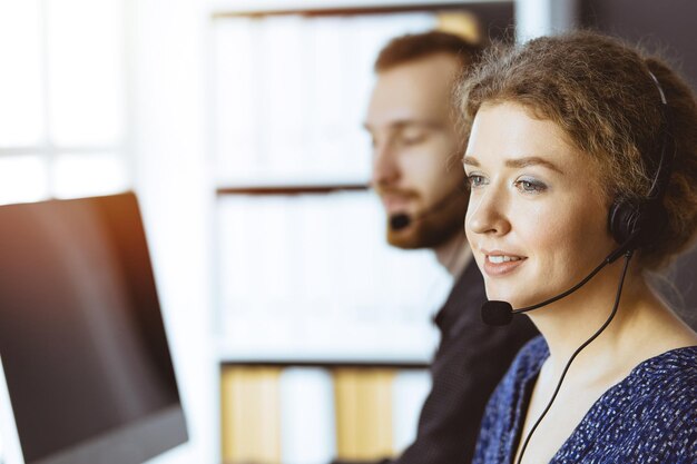 Mulher de negócios falando pelo fone de ouvido enquanto está sentado com o colega ruivo no escritório ensolarado moderno. grupo de pessoas diversas no call center.