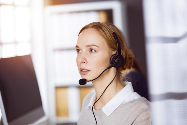 Mulher de negócios falando pelo fone de ouvido no escritório. Call center e grupo diversificado de pessoas nos negócios.