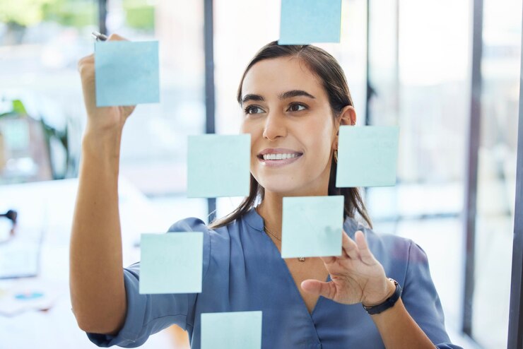 Foto mulher de negócios fazendo brainstorming e planejando agenda para metas agenda e visão na janela do escritório feliz jovem trabalhador escrevendo ideias de notas adesivas e estratégia para empresa em agência de inicialização
