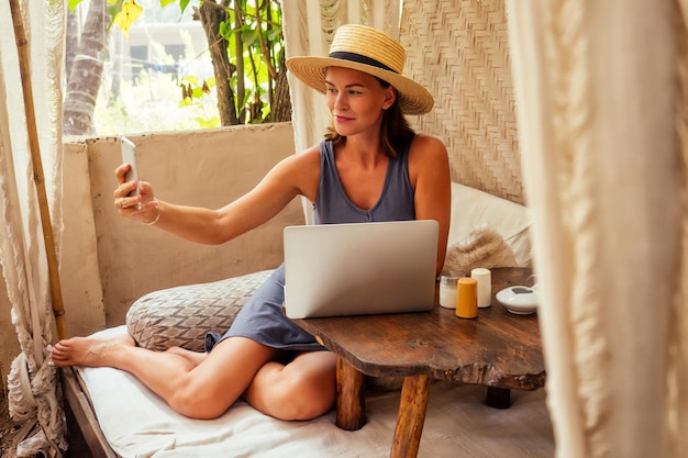 Mulher de negócios feliz bem-sucedida usando laptop e telefone como freelancer na praia do paraíso tropical. Garota xícara chá, café freelancer, trabalhando, sentada em um café de verão, trabalho remoto, oceano Índico