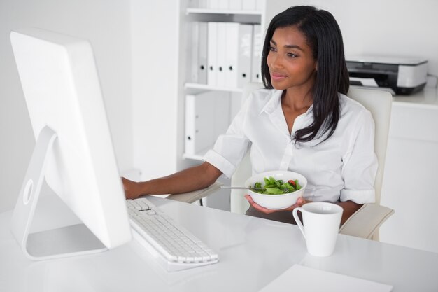 Mulher de negócios feliz bonita comendo uma salada em sua mesa