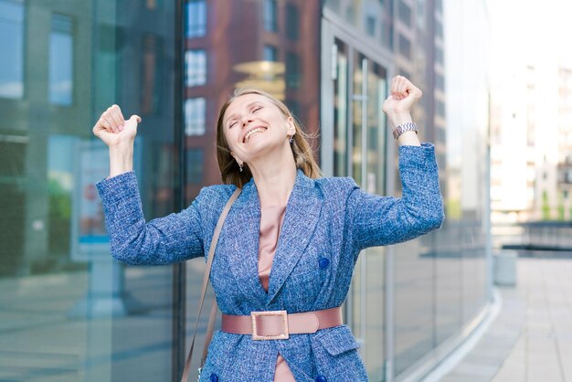 Foto mulher de negócios feliz mostrando os polegares enquanto está ao ar livre contra o escritório