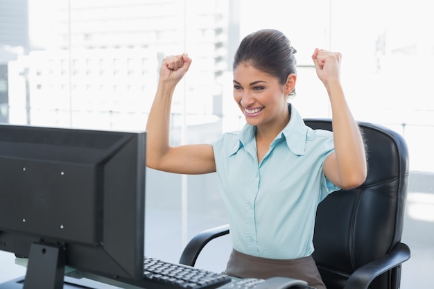 Mulher de negócios feliz que olha o computador no escritório