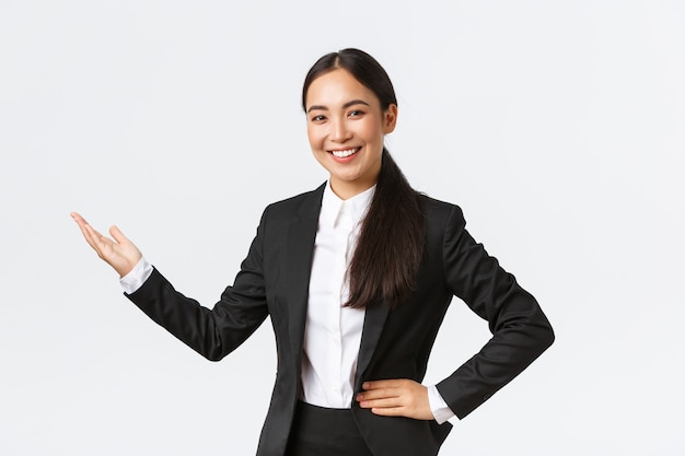 Mulher de negócios feliz sorridente em um terno preto apontando com a mão esquerda para as estatísticas do diagrama com rosto satisfeito, tendo uma reunião de negócios, apresentação de produto ou gráfico, fundo branco de pé