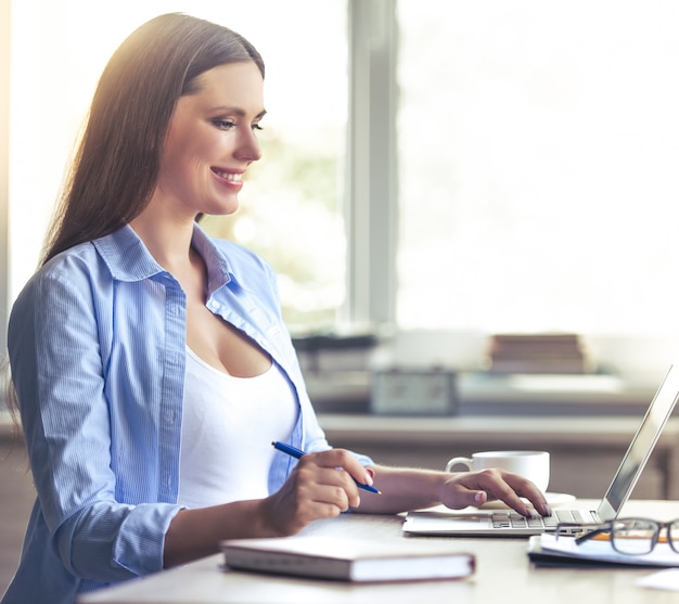 Mulher de negócios grávida bonita está usando um laptop.